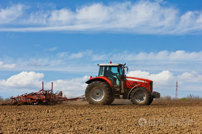 种田的农民。在该字段中的培养拖拉机。红色农用拖拉机用在农田中犁。拖拉机和犁